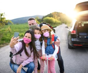 Front view of family with two small daughters on trip outdoors in nature, wearing face masks.