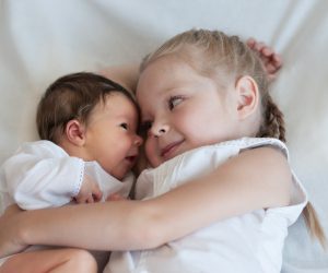 5 years old sister hugs her younger 2 weeks old brother